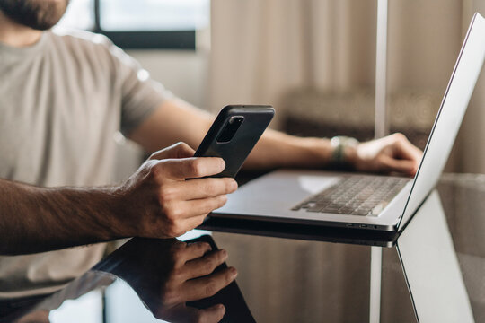 Man reading message on smartphone and using laptop