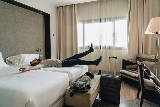 Relaxed man jumping on bed in hotel room