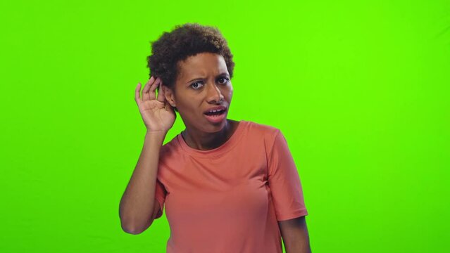 Young beautiful ethnic African American woman millennial listens and starts laughing at joke of interlocutor feels positive emotions in conversation posing in studio on green background