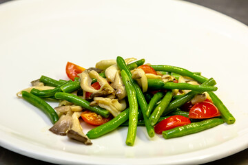 Fried oyster mushrooms with green string beans and tomatoes are on a plate