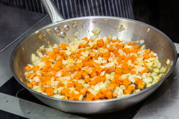 The cook is frying onions and carrots cut into thin slices in a frying pan