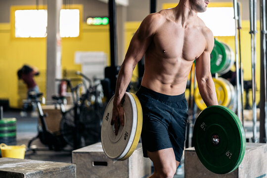 Shirtless sportsman carrying barbell discs