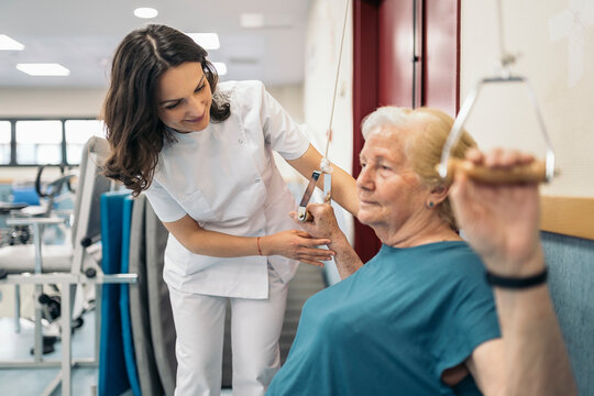 Happy physiotherapist helping elderly patient