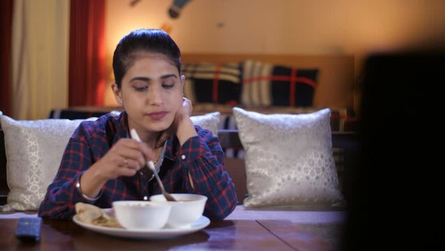 A young girl is eating healthy homecooked food while watching television - leisure time  fun and entertainment. A beautiful lady in casual clothes using a remote control to switch Tv channels while...