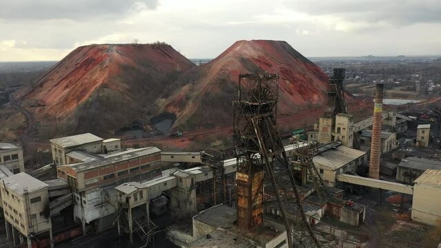 Old coal mine elevator and slag heaps on a cloudy day. Vintage coal mining shaft building, weathered factory and constructions. Fossil fuel and minerals mining heavy industry landscape with terrikons.