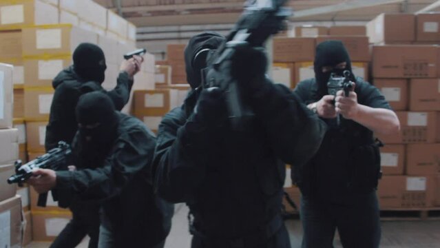 A special forces military team raid a warehouse with guns drawn wearing balaclavas an gas masks
