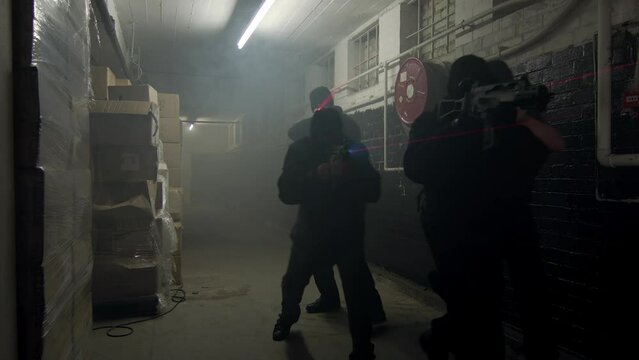 A unit of swat special forces enters a smokey warehouse with laser sights on their guns