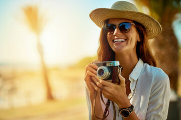 Ready for summer and new memories. Shot of an attractive young woman using a camera on a summers day outdoors.