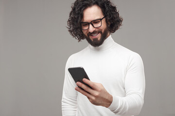 Smiling curly haired man browsing smartphone in studio