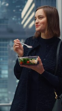 Vertical Screen: Confident Young Female Riding Glass Elevator to Office in Modern Business Center and Eating Healthy Salad with Vegetables. Happy Manager Preparing for Productive Day at Work.