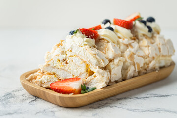 Meringue roll decorated with strawberries and blueberries sliced and served in the wooden plate on the white background. Macro shot