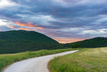 Sunset dramatic sky over country road in Marche region, Italy. Epic clouds above winding trail...