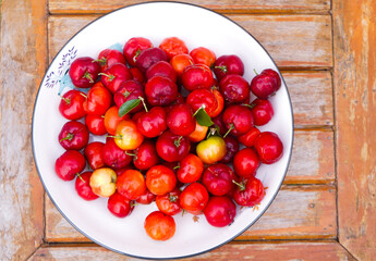 Acerola cherry in white bowl on white wooden background.