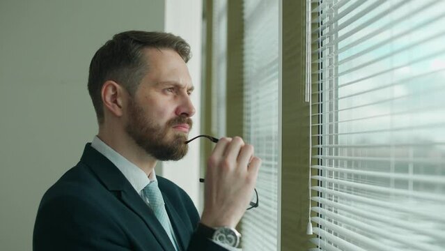 Thinking process, focused businessman in a suit stands at the panoramic window in the office and reflects, the thought process, natural lighting.