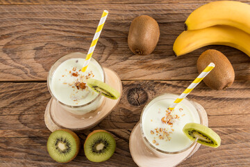 top view of two glasses of homemade fruit smoothies with nuts standing on a natural podium made of wood and a rustic table .