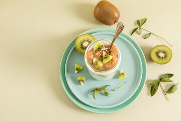 smoothie with kiwi, banana and nuts in a modern glass on a ceramic plate and a beige background with kiwi slices. detox healthy food for energy.