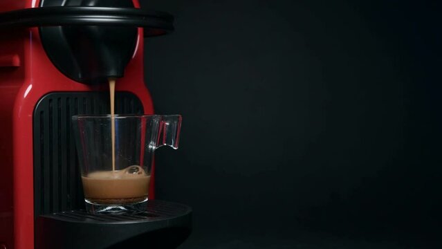 Process of making coffee by coffee machine into glass transparent cup - espresso coffee coming out from home coffemaker machine - On black background 