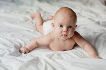 cheerful smiling newborn baby in a diaper lies on his stomach on a white bed