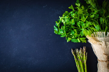 Obraz na płótnie Canvas Bunch of parsley, dill, coriander and asparagus on black table