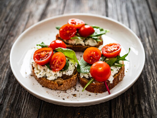 Tasty sandwiches - toasted bread with cream cheese, cherry tomatoes and green leaves on wooden table
