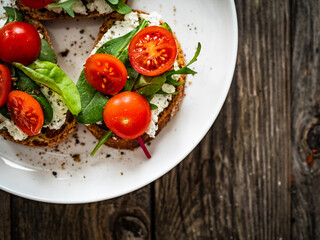Tasty sandwiches - toasted bread with cream cheese, cherry tomatoes and green leaves on wooden table
