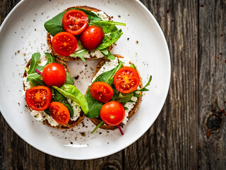 Tasty sandwiches - toasted bread with cream cheese, cherry tomatoes and green leaves on wooden table
