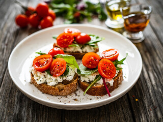 Tasty sandwiches - toasted bread with cream cheese, cherry tomatoes and green leaves on wooden table
