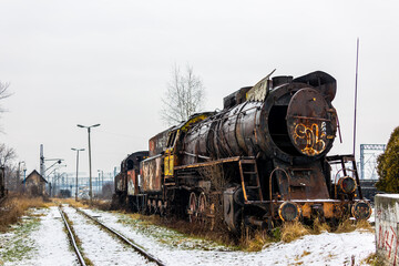 Old, rusty, demolished steam locomotive standing on the side track of the train station. Picture taken in cloudy winter day.