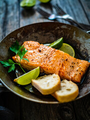Fried salmon steak with bread and lime in frying pan on wooden table