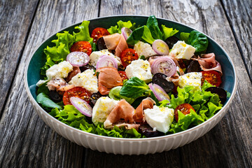Tasty salad - prosciutto di Parma, manouri cheese and fresh, green vegetables on wooden table