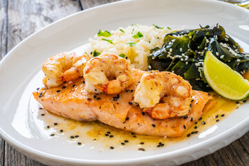 Fried salmon steak with prawns, white rice and spinach on wooden table
