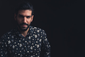 young attractive bearded Hispanic man looking suspicious into the camera copy space black background studio shot medium closeup. High quality photo