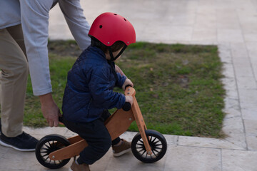 Father teaching his toddler boy to ride a balance bike for the first time. Red helmet.