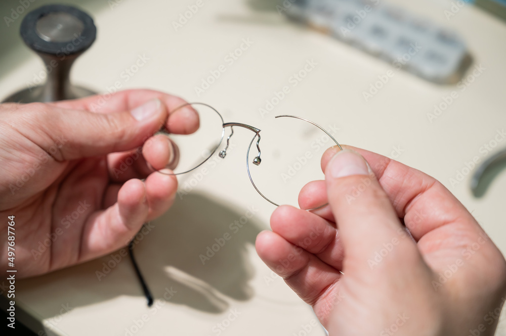 Wall mural A man repairs a broken eyeglass frame. Close-up of the ophthalmologist's hands