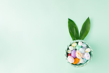 Easter basket with eggs and rabbit ears made of natural leaves on a pastel green background. Minimal holiday flat lay compositin.