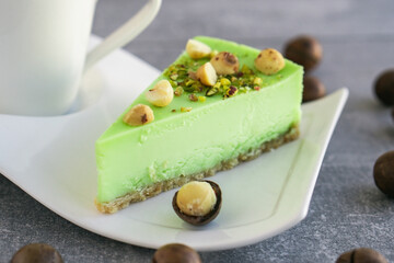 Green pistachio cake with macadamia nuts on white plate with cappuccino. Creamy pistachio cheesecake