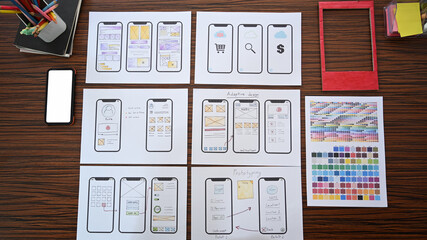 Flat lay creative designer workplace with wireframe sketches for mobile application on wooden table.