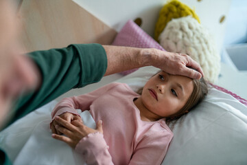 Grandfather taking care of his ill granddaughter lying in bed.