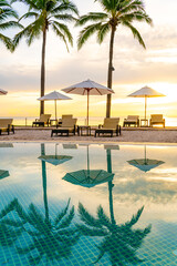 Umbrella and chair around swimming pool in hotel resort with sunrise in morning