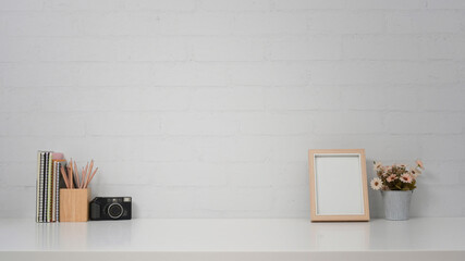 Creative workplace with camera, picture frame and flower pot against brick wall. Copy space for your advertise text.