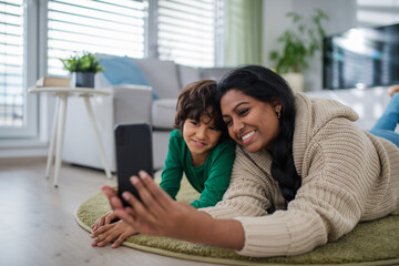 Indian mother lying on floor with her little son at home, taking selfie.