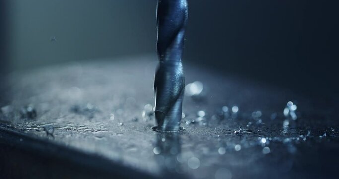 Macro shot of tip of drill machine drilling hole with circular motion with silver metal shavings during steel machining process in heavy industry factory.