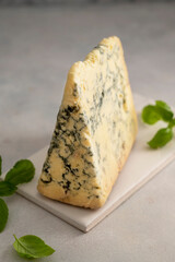 Blue cheese piece with fresh basil leaves over gray background. One triangle of cheese.