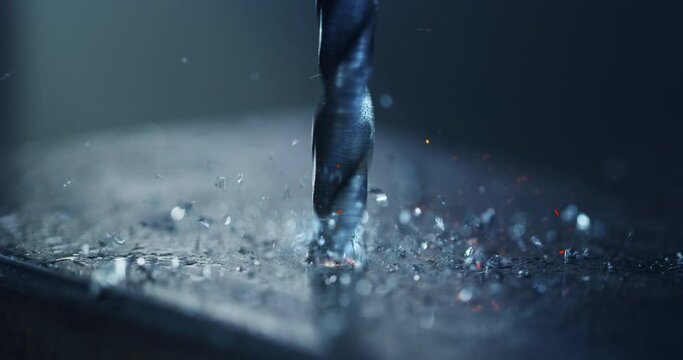 Macro shot of tip of drill machine drilling hole with circular motion with silver metal shavings during steel machining process in heavy industry factory.