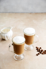 Coffee in glass ?ups with whipped milk foam on neutral background. Copy space for text.