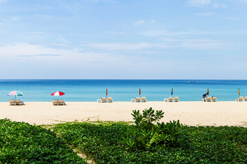 Sunbed and umbrella over blue sea and sandy beach with green plant, nature background, tropical island, summer outdoor day light