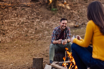 Smiling man talking to woman, sitting near the campfire.