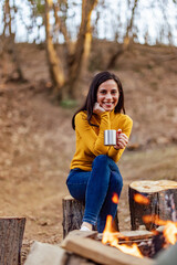 Portrait of a brunette woman, sitting on the log, drinking her coffee.