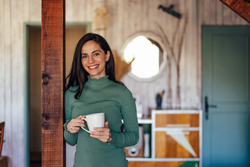 Portrait of a smiling brunette woman, looking at the camera, holding a cup of coffee.