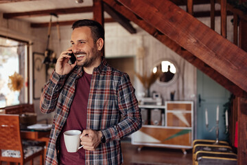 Smiling man making a phone call, talking to someone while drinking coffee.
